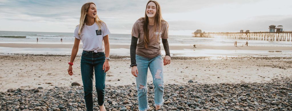 Two girls walking away from the ocean. They are smiling and laughing.