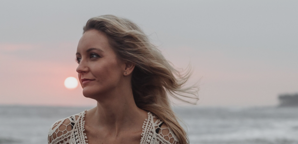 A woman, looking into the distance in front of the ocean.
