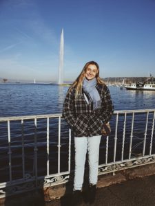 Bella, pictured in front of a body of water in which there is a large, man made fountain.