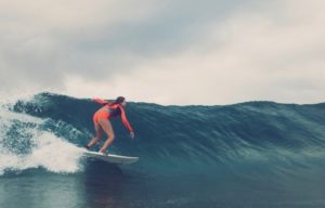 Bella, surfing a smooth wave in an orange summer wetsuit.