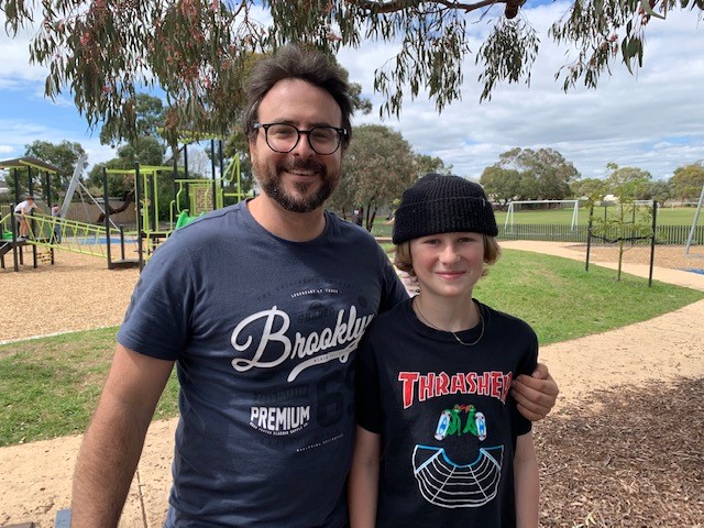 A man and a boy, pictured in front of a playground and smiling at the camera.