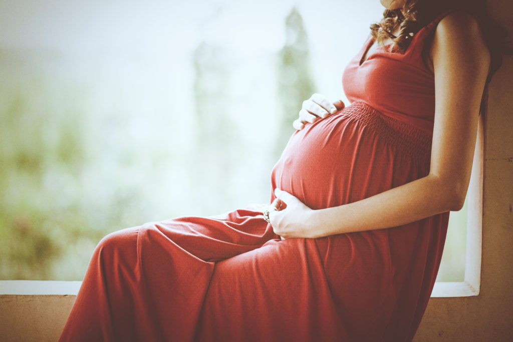 A pregnant woman in a red dress. She is holding her belly.