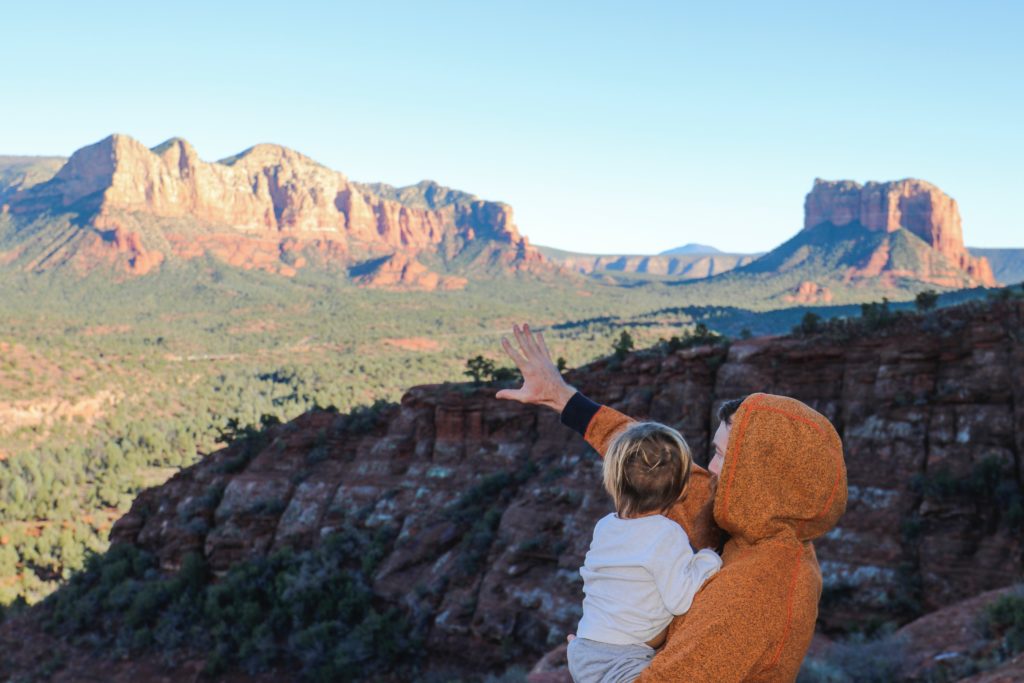 A man holding a child and looking out over a rugged and hilly landscape.