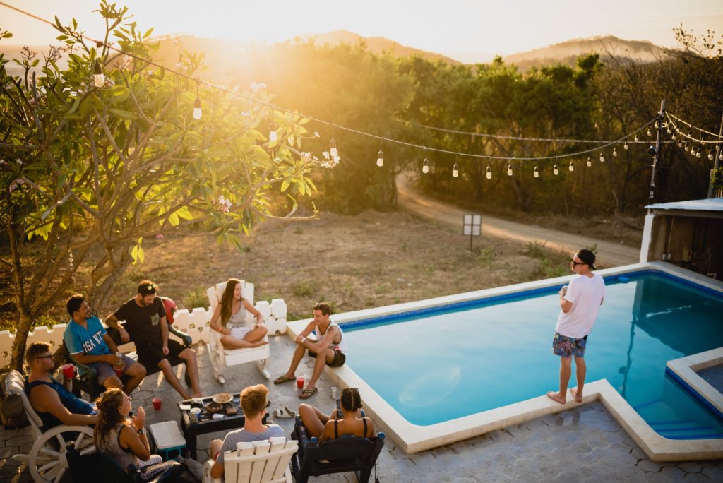 A group of people, captured from above. They are socialising around a pool.