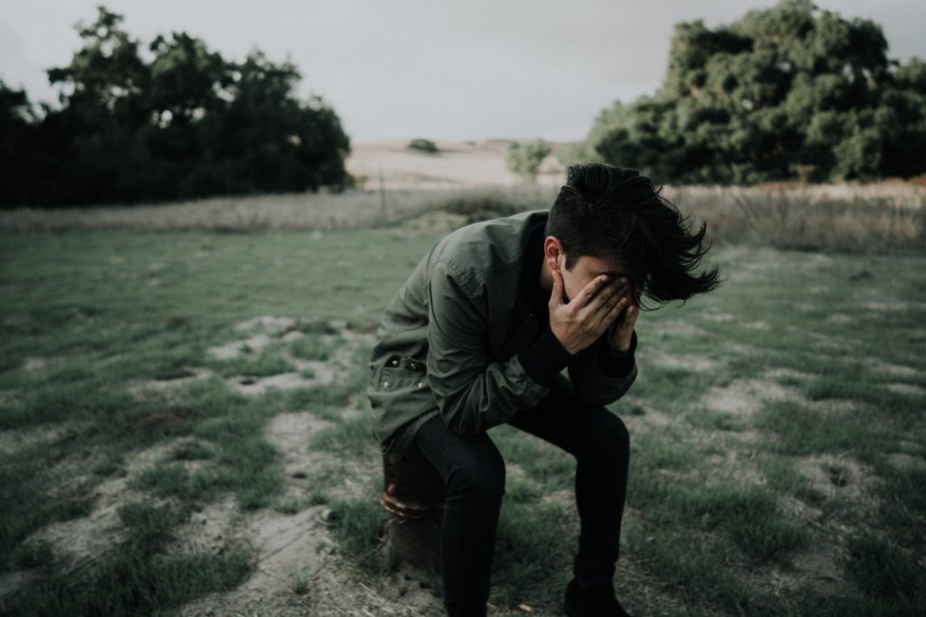 A man, sitting down outside with his head in his hands.