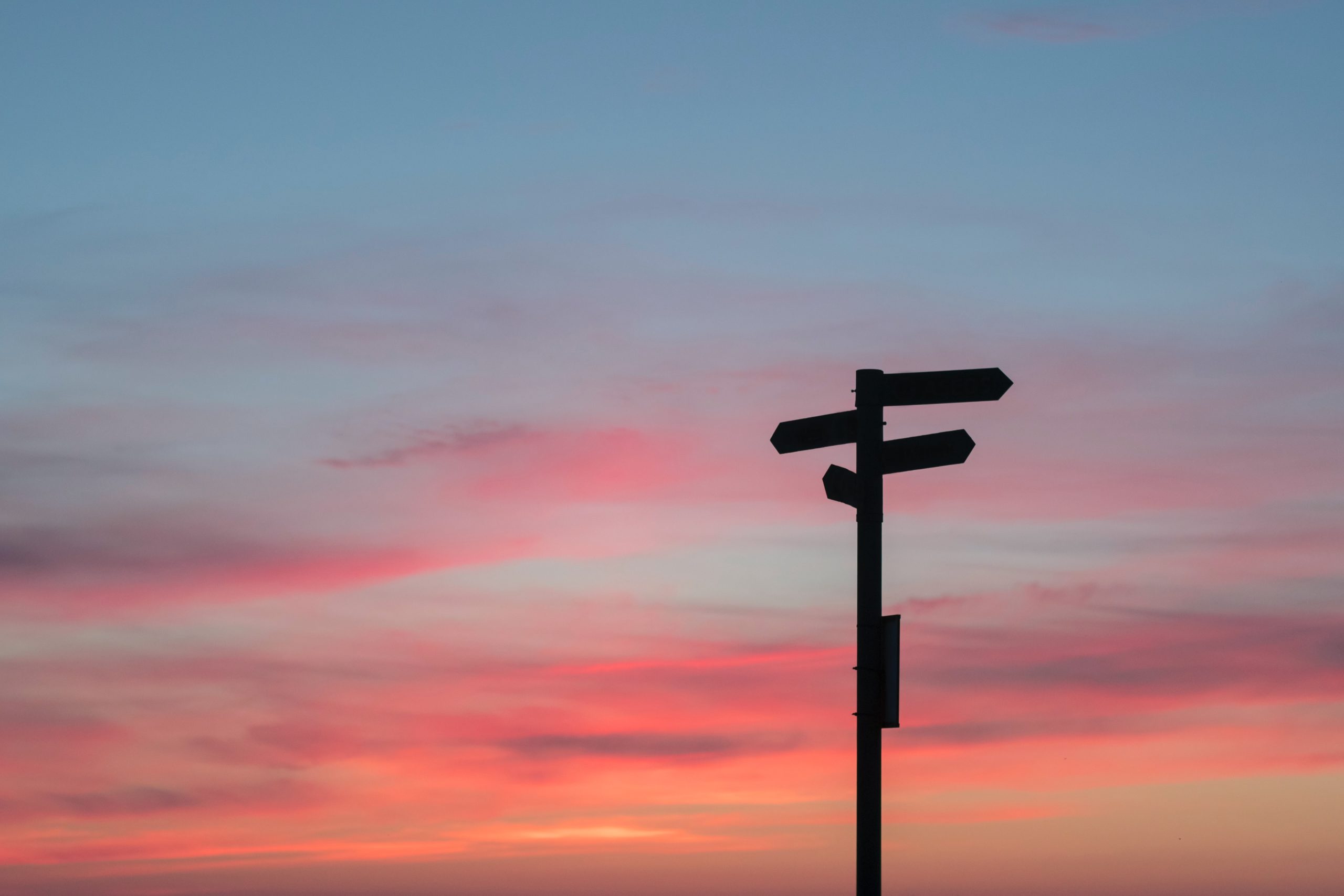 A silhouette of a signpost, with a brightly coloured sky at sunset behind it.