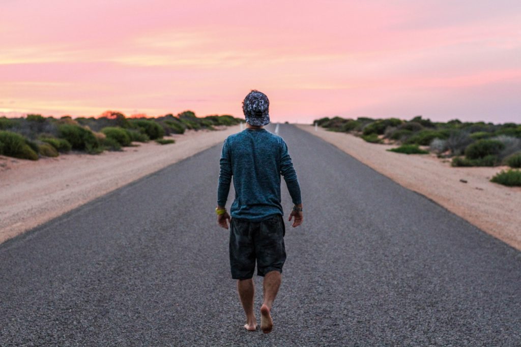 Growth Mindset | A man walking along a road, shown from behind. The sky is pink and he appears to be in a desert.