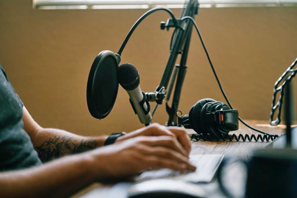 A man sitting at table. In front of him is equipment used for recording a podcast.