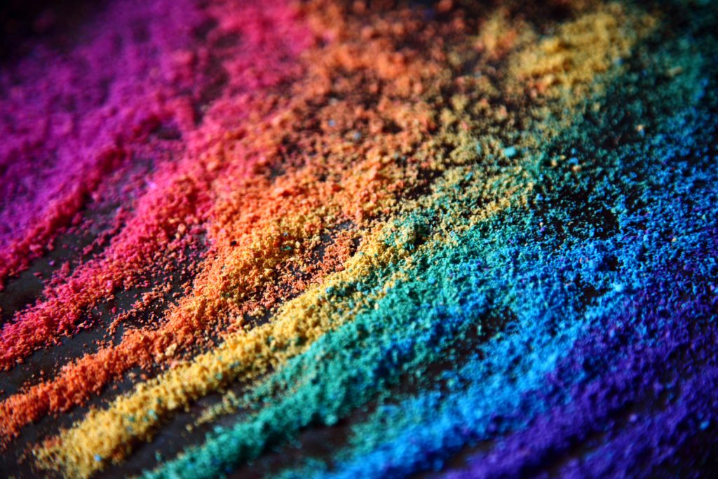 Different colours of sand spread out in rainbow order on a dark surface.