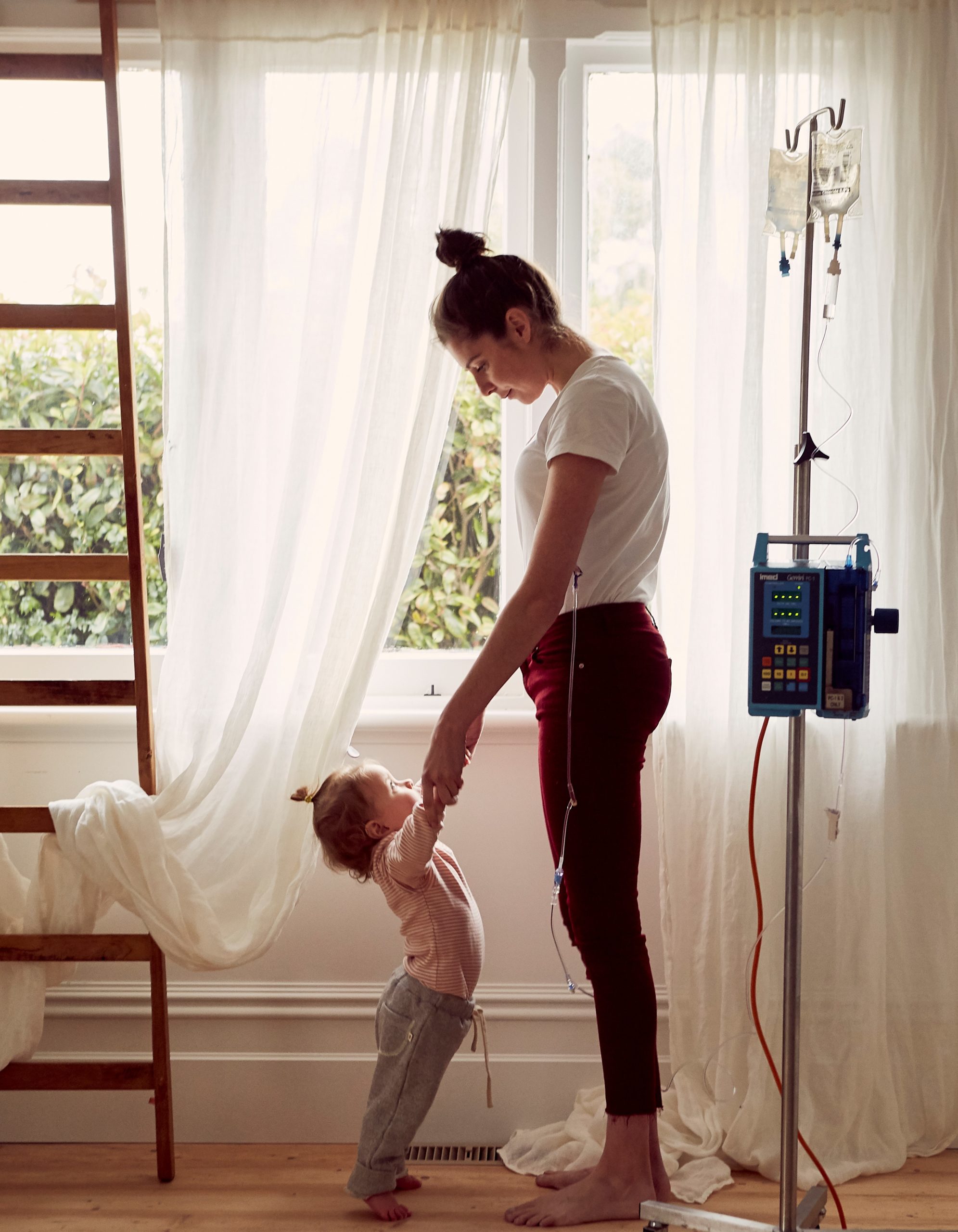 Alex and her child, facing each other and holding hands. Alex is connected to a medical device.