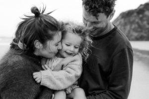 Alex, her partner and her child. They are pictured smiling, outside in greyscale.