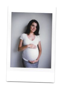 Alex during her pregnancy. She is holding her belly and wearing a white t-shirt.