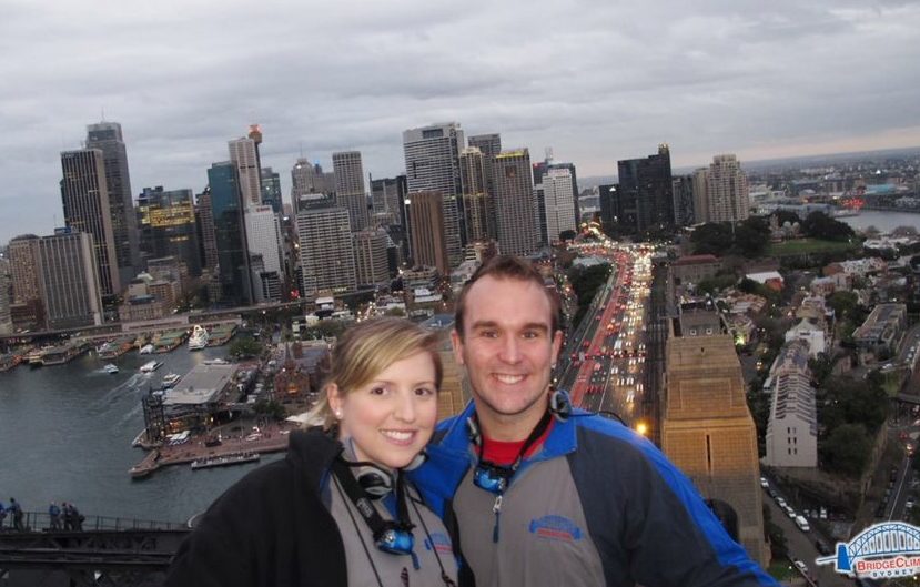 Catherine and her partner, pictured on top of the Sydney Harbour Bridge after completing the bridge climb. The city of Sydney is pictured in the background.