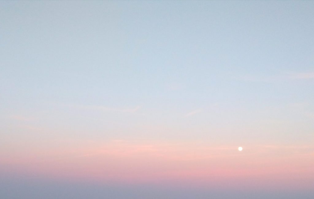 The sky, coloured light blue, orange and purple. The sun is a small bright spot in the image.