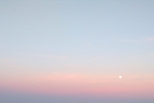 The sky, coloured light blue, orange and purple. The sun is a small bright spot in the image.