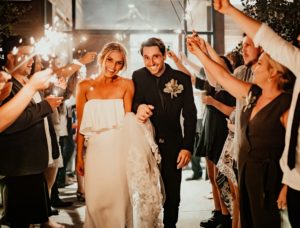 Jess and her partner walking in between guests at their wedding. The guests are holding up sparklers.