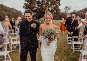 Jess and her partner at their wedding. Jess is holding a bouquet and smiling at the camera as they are showered in confetti by guests.