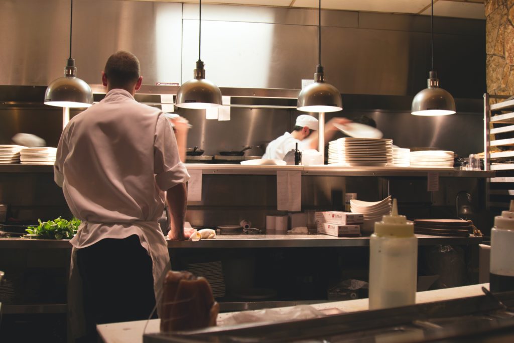 A few chefs working inside a kitchen. There are lights hanging down from the ceiling.