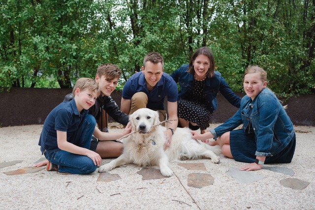 Serena and her family of five outside, sitting around their white golden retriever on pavement.