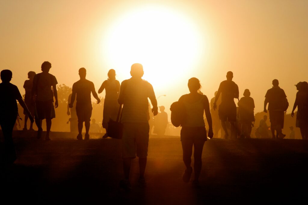 A large group of people, with only their silhouettes shown due to the sun rising/setting behind them.