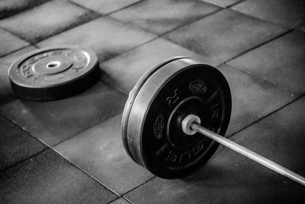 One side of a barbell. with some weights on the end, resting on a dark floor.