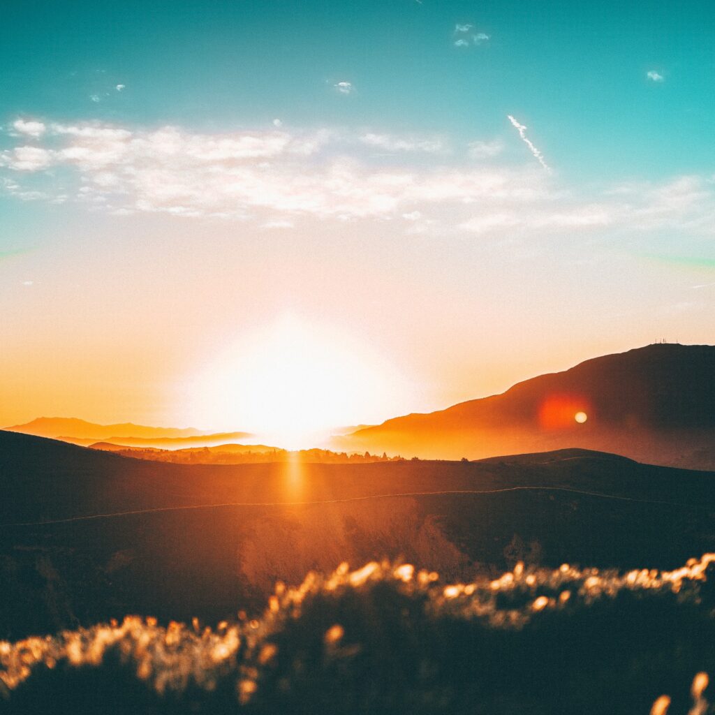 The sun rising or setting over a landscape of rolling hills. The sun cast an orange glow across the image.