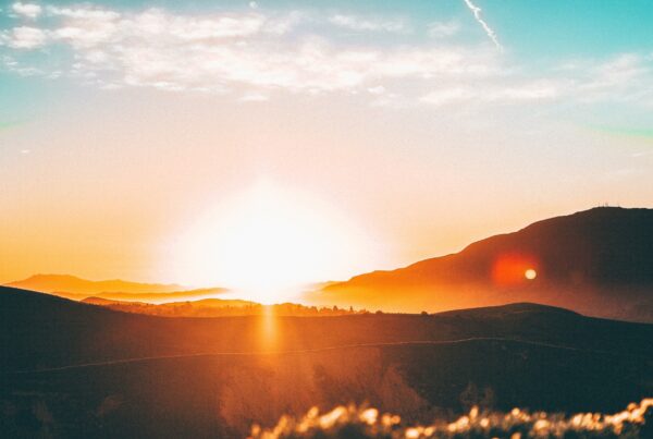 The sun rising or setting over a landscape of rolling hills. The sun cast an orange glow across the image.